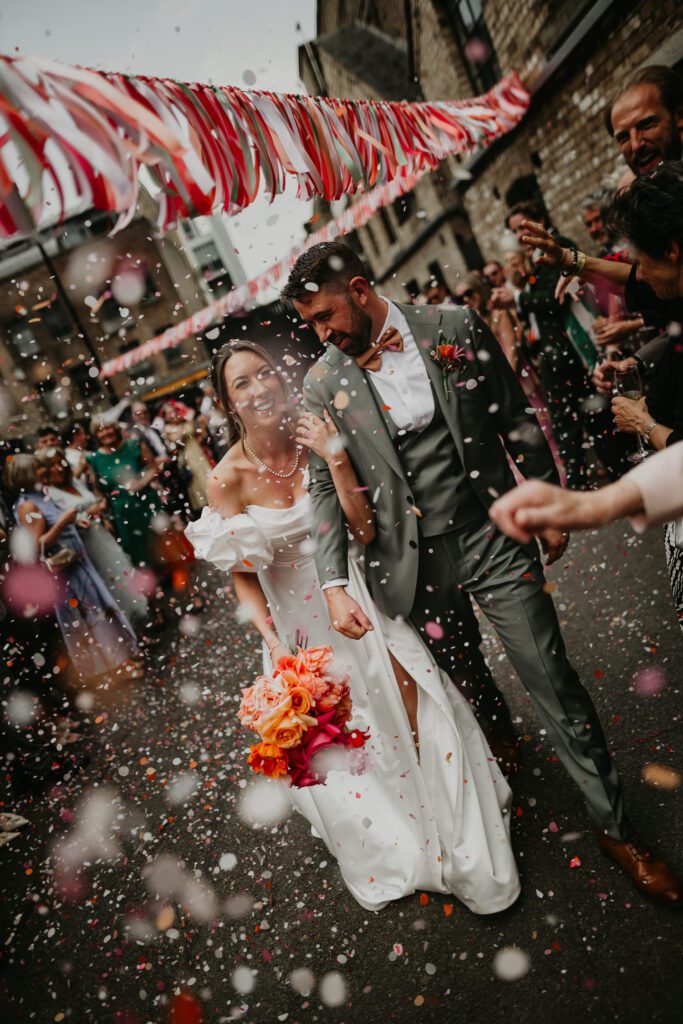 A bride and groom walk into Shoreditch Studios as their guests throw biodegradable wedding confetti at their Eco-Friendly Wedding. 