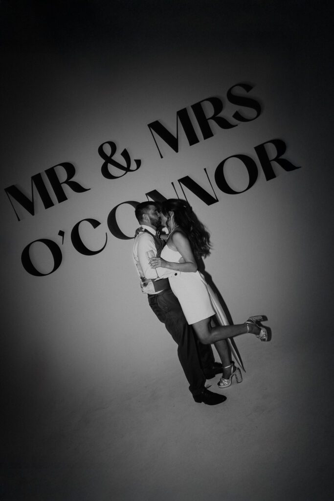 Bride and groom kiss in front of their last name decal on the wall of Shoreditch Studios where they had their London wedding.