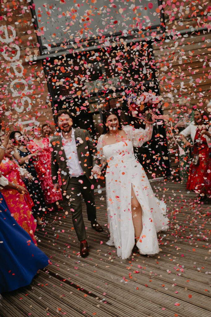 A bride and groom walk out of their wedding ceremony at their Eco-Friendly Wedding to be showered in biodegradable wedding confetti. 